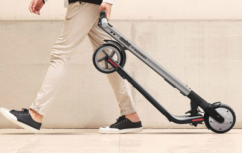 Man wheeling the ES2 electric scooter in its folded position